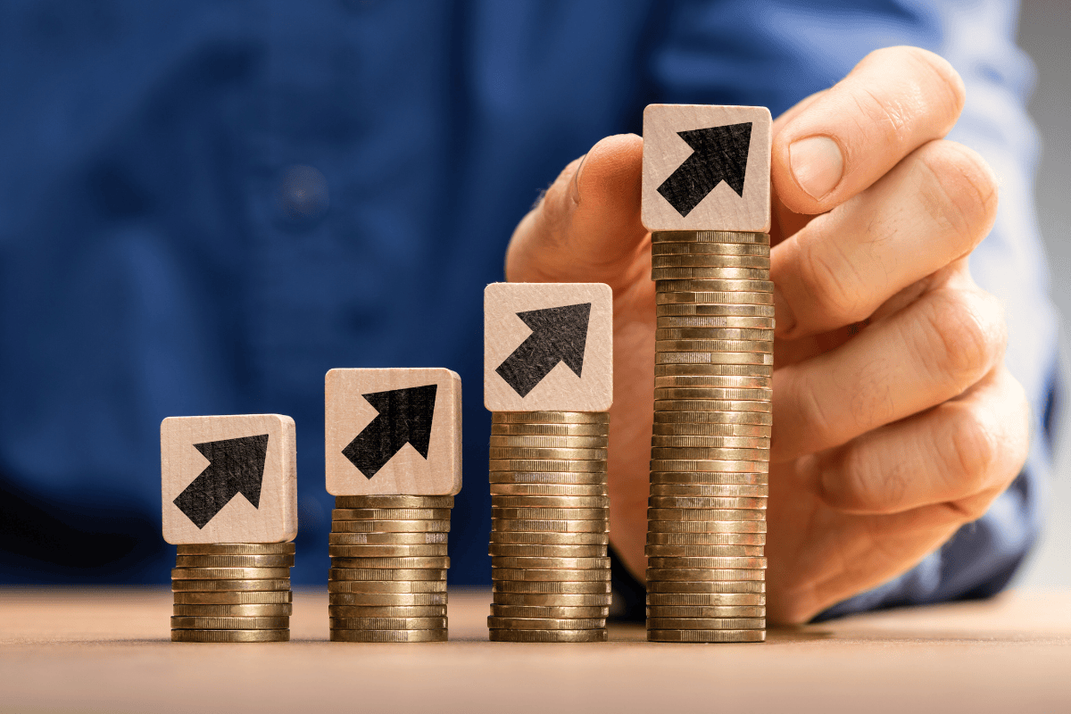 Mano empresarial señalando cuatro pilas crecientes de monedas doradas con flechas ascendentes, simbolizando el crecimiento salarial y aumentos de sueldo progresivos